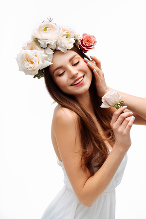 Beautiful young girl smiling and posing with flowers on white background in white dress. Studio portrait.の写真素材