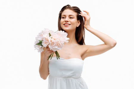 Portrait beautiful young girl smiling and posing with artificial flowers on white background in white dress.の写真素材