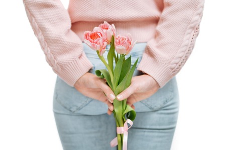 young woman holding of pink tulips behind her back on a white background.の写真素材