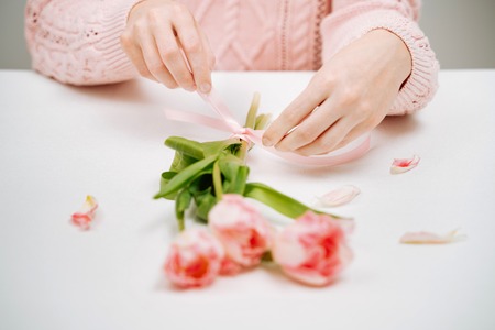 Young woman tying a ribbon on a bouquet of pink tulips.の写真素材