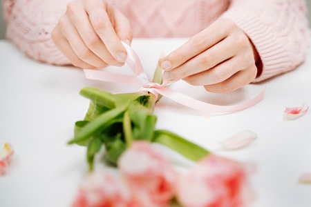 Young woman tying a ribbon on a bouquet of pink tulips.の写真素材