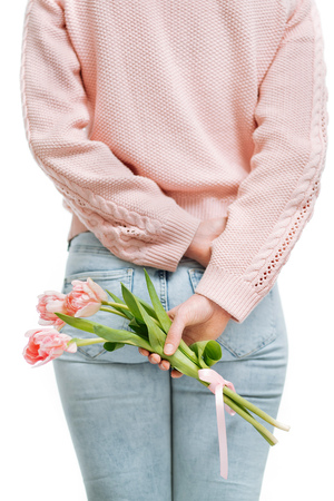 young woman holding of pink tulips behind her back on a white background.の写真素材