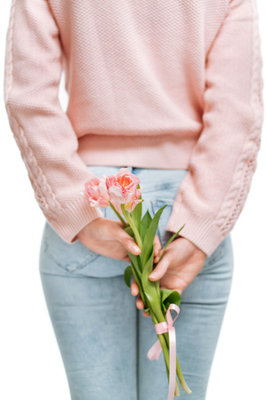 young woman holding of pink tulips behind her back on a white background.の写真素材