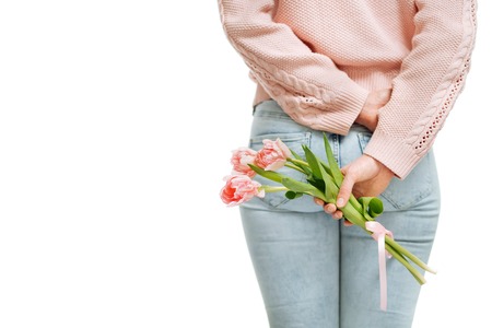 young woman holding of pink tulips behind her back on a white background.の写真素材