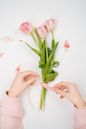 Young woman tying a ribbon on a bouquet of pink tulips.の写真素材