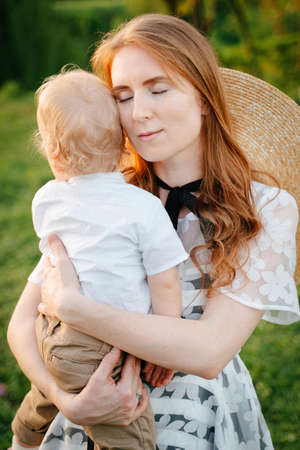 A gentle calm red-haired mother with a child soothes and hugs her sons boy in her arms. Mothers Day.