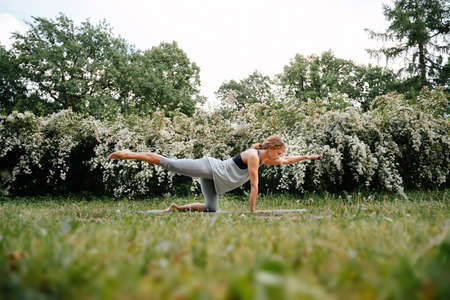 Young red-haired woman performs exercises for the spine and posture in the park. Lotus position in yoga.の写真素材