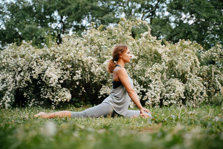 Young slender girl goes in for sports, doing exercises in yoga equestrian pose outdoors in the park. Horizontal stretching exercises.の写真素材