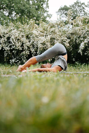 Young slender girl meditates in the park on the green grass. Performing exercises in yoga.の写真素材
