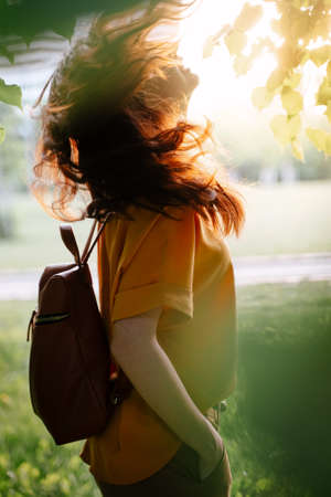 Portrait of a beautiful girl in a yellow sweater at sunset, the wind develops dark hair against the background of green nature. Summer time.の写真素材