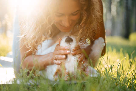 A woman plays with her terrier dog on a green backyard lawn in sunny weather.の写真素材