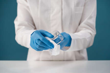 Close-up of a medical worker in blue latex gloves, safety goggles after a sick patient. Treatment with a rag and a chemical solution of a medical product.の写真素材