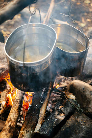Close-up of a vertical aluminum cookware in soot over a campfire for making soup in a field.の写真素材