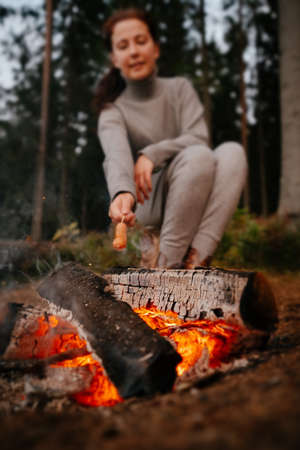 Young female tourist cooking barbecue sausages on a campfire. Selective focus on fire.の写真素材