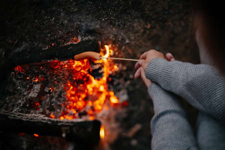 Sausages fried on a fire on a wooden rod in a summer forest. Concept of tourism and camping.の写真素材