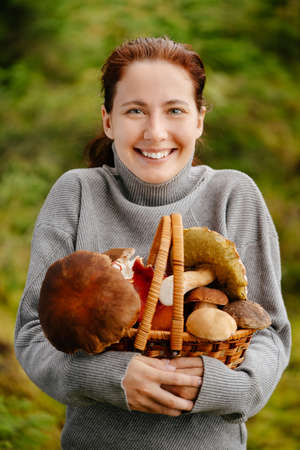 Portrait of a young woman with a brown basket and fresh edible mushrooms. The concept of hiking and ecotourism.の写真素材