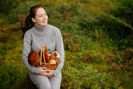 Woman is resting in a green forest with bascket of mushrooms. Concept of ecotourism.の写真素材