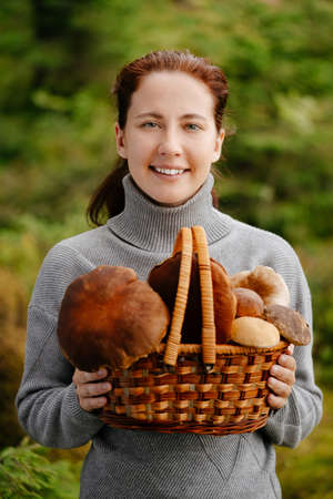 A happy woman with a basket of mushrooms in the forest. Portrait of a forester with a harvest.の写真素材