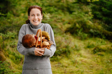 Happy young woman on the background of a green forest holds a wicker basket with mushrooms. Concept of organic food.の写真素材