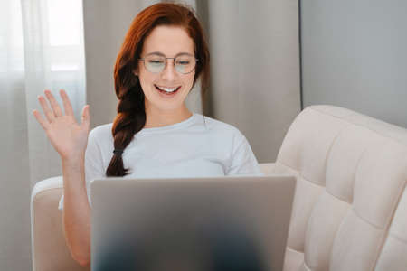 Young woman smiling greets friend and colleague by video link while sitting at home laptop.The concept online communication.の写真素材