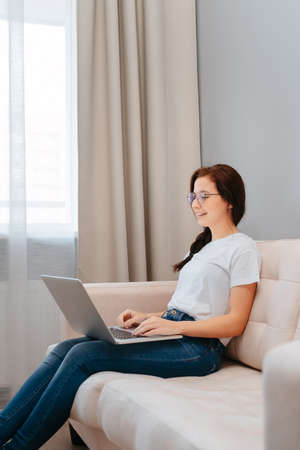 Young female student at distance learning and work is sitting on a bright sofa with a laptop.の写真素材