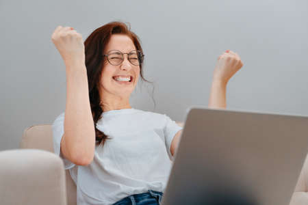 Young woman emotionally rejoices at the victory holding a laptop. Concept of freelancer and lottery.の写真素材