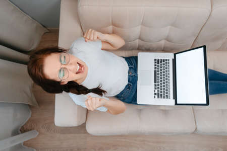 Young angry woman with glasses using a laptop at home in the living room is sitting on the sofa. Work at home in quarantine isolation.の写真素材