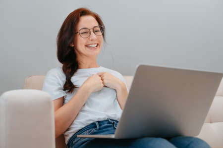 Young smiling woman with glasses communicates with friends and colleagues on the Internet while sitting at home in the living room.の写真素材