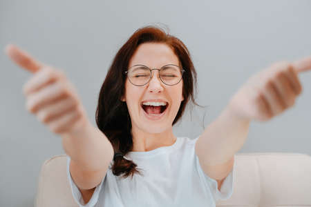 Young woman with glasses close-up is happy with a perfectly done job showing blurred thumbs up.Concept of good service.の写真素材