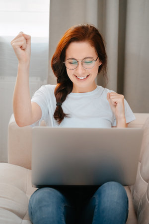 Young woman smiling looks at the laptop screen celebrates the victory and shows a yes gesture. The concept of winning the lottery.の写真素材