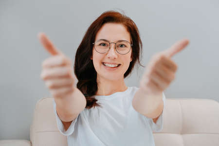 Smiling young woman close-up with glasses gives a thumbs up recommends goods and services.の写真素材