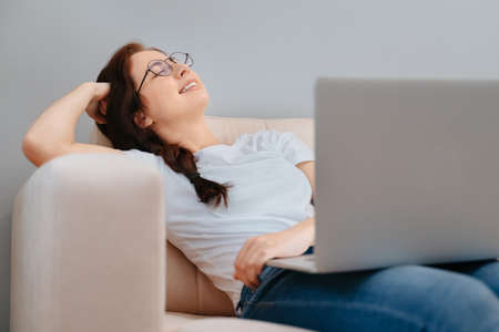 Young happy freelance woman is resting on the couch with a laptop.Concept of working and studying at home.の写真素材