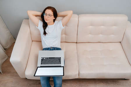 Young woman sitting on the couch at home is resting after finishing work on a laptop. Concept of freelancer and online training.の写真素材