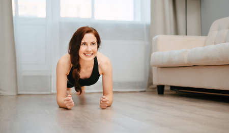 Young woman is engaged in fitness at home doing a plank exercise. Concept of sports.