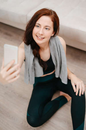 Young woman in sportswear takes a selfie on her phone after doing sports at home.Concept of fitness.の写真素材