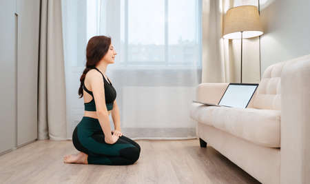 Young female athlete is sitting at home in the living room studying fitness lessons on a laptop.の写真素材