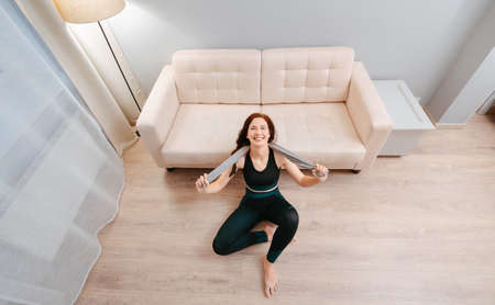 Athlete is sitting on the floor in the living room top view tired after a fitness class at home.Concept of sport and health.の写真素材