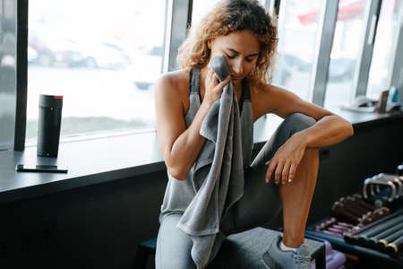 Tired female athlete after an active body workout rests wiping sweat with a towel in the gym. Concept of fitness and weight loss.の写真素材