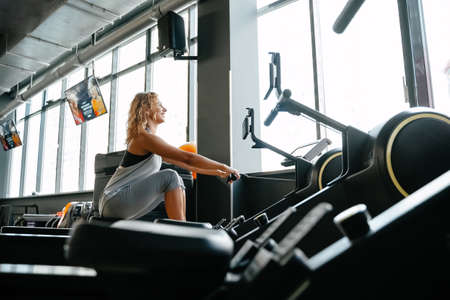 Happy athletic woman is engaged in rowing in the gym for muscle training. Concept of fitness and weight loss.の写真素材
