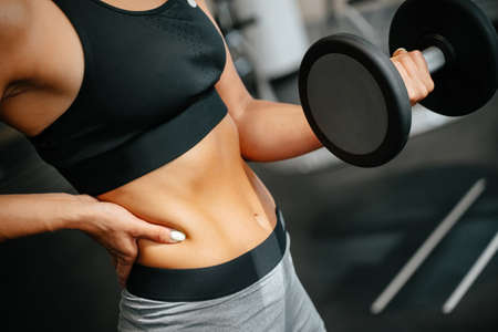 Slender woman is engaged in fitness lifting dumbbells exercises for muscles of arms. Concept of sports lifestyles.の写真素材