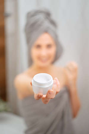 White jar with a cream for wrinkles and moisturizing the skin in the hands of a girl blurred in the bathroom.の写真素材