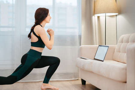 Young woman is engaged in remote yoga or stretching using a laptop at home. Fitness in the apartmentの写真素材