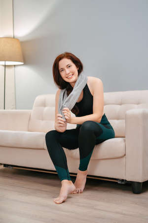 Woman in sports clothes is sitting tired after a yoga workout at home. Concept of weight loss and a healthy lifestyleの写真素材