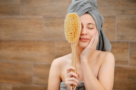Portrait of a young woman in the bathroom with a wooden brush for body massage from cellulite and stretch marks.の写真素材