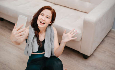 Young female trainer is welcomed by yoga and fitness students online by phone.Concept of online learning and sports.の写真素材