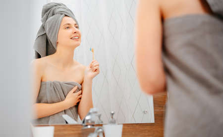 Young woman in a towel brushes her teeth in the bathroom. Morning body care.の写真素材