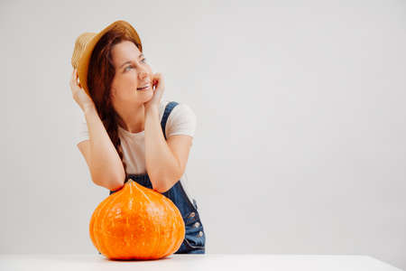 Woman in a wicker hat stands on a white background with a large orange pumpkin for the Halloween holiday.の写真素材