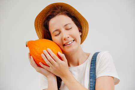 Farmer woman in overalls and a hat clutches a ripe orange pumpkin. Concept of vegetarianism and agriculture.の写真素材