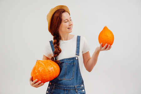 Young woman holds a crop of orange pumpkins on a white background while looking at one. Concept of the harvest season.の写真素材