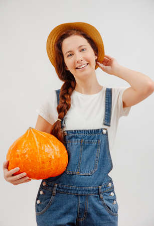 Young farmer woman smiles with an orange ripe pumpkin on a white background. Concept of gardening and halloween.の写真素材